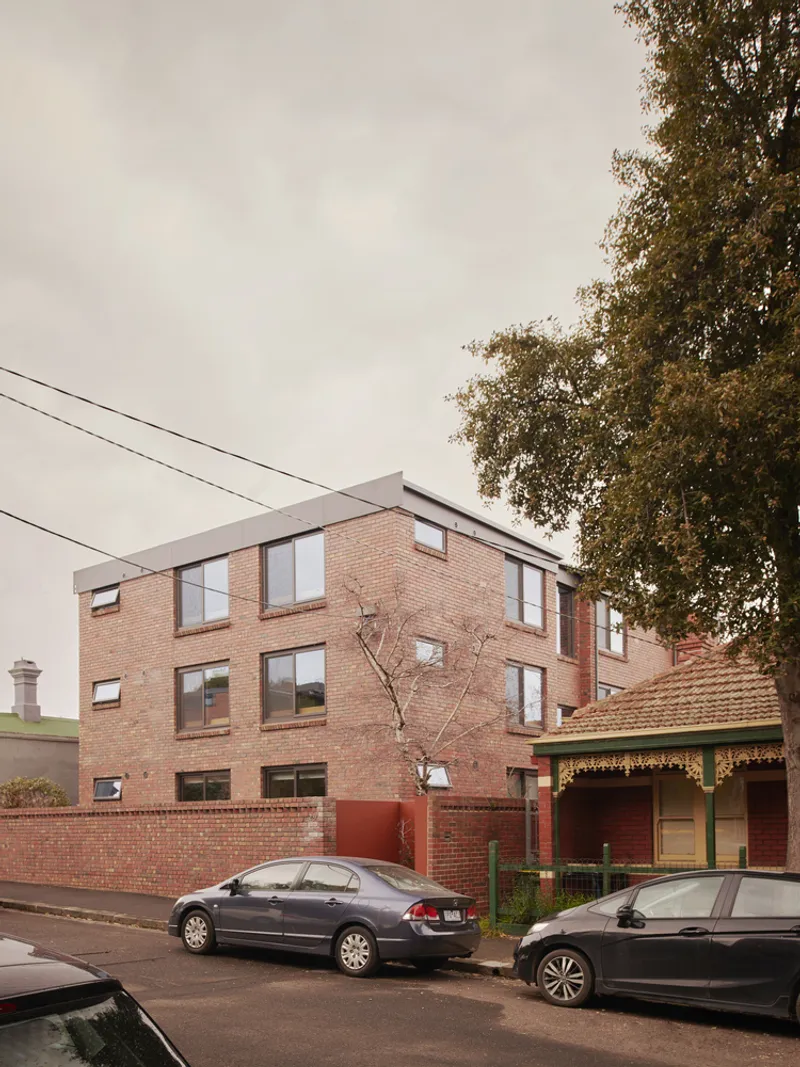 Street view of the three-storey brick facade with a bare tree and parked cars under an overcast sky
