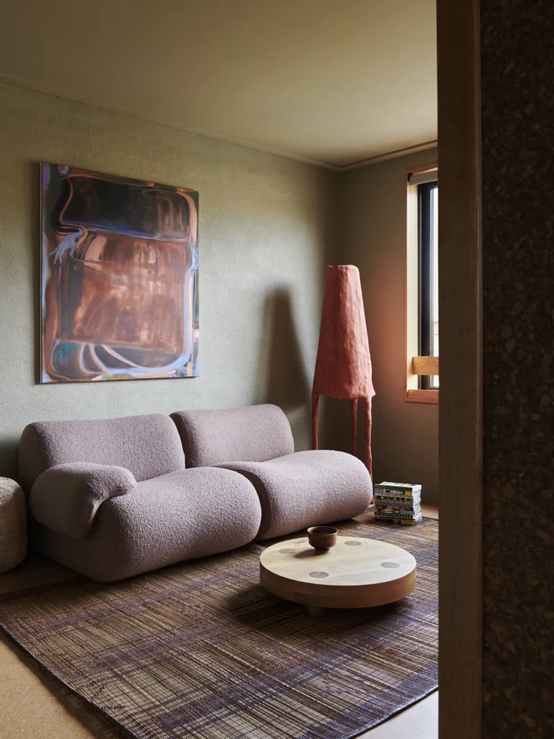 Living room with textured sofa and conical lamp in afternoon sunlight filtered through a narrow window