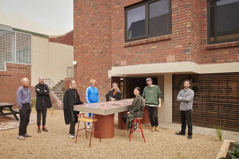 Courtyard with group of eight residents gathered around the outdoor laundry counter and gravel paving