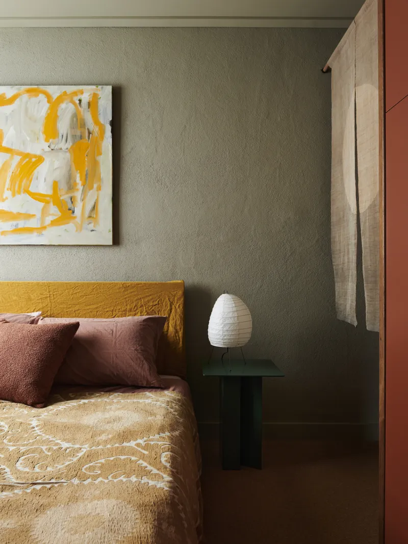 Bedroom corner with sage green walls, timber sliding door jamb and dark glass bedside table with white lamp