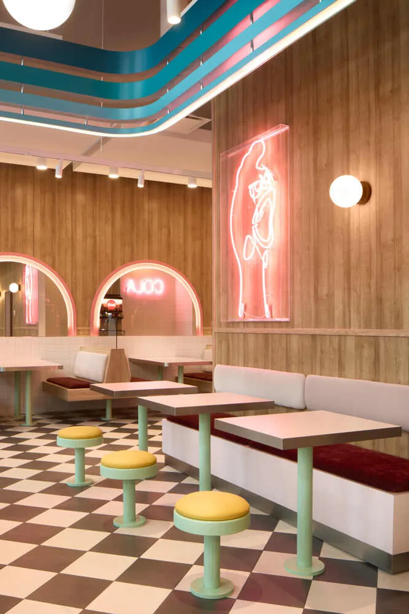 Banquette seating with yellow stools and pink neon figure mounted on vertical wood panels