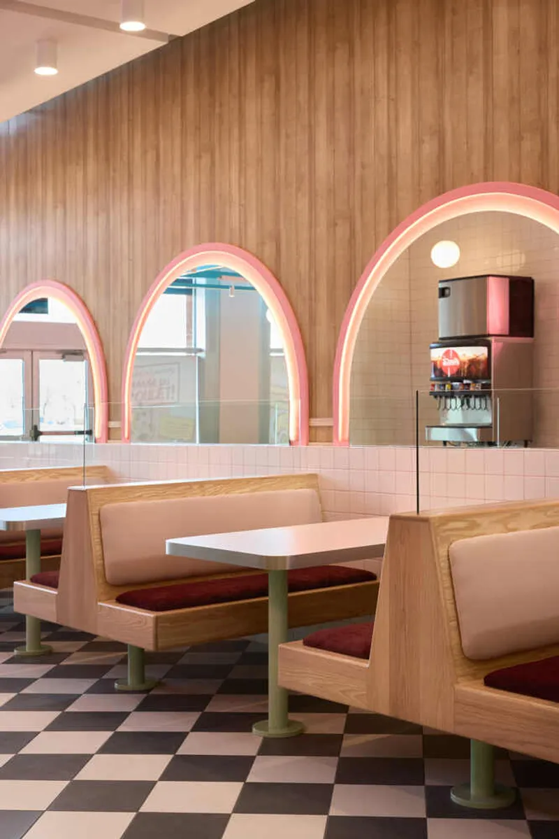 Booth seating with blonde wood frames and pink neon arches reflected in glass behind