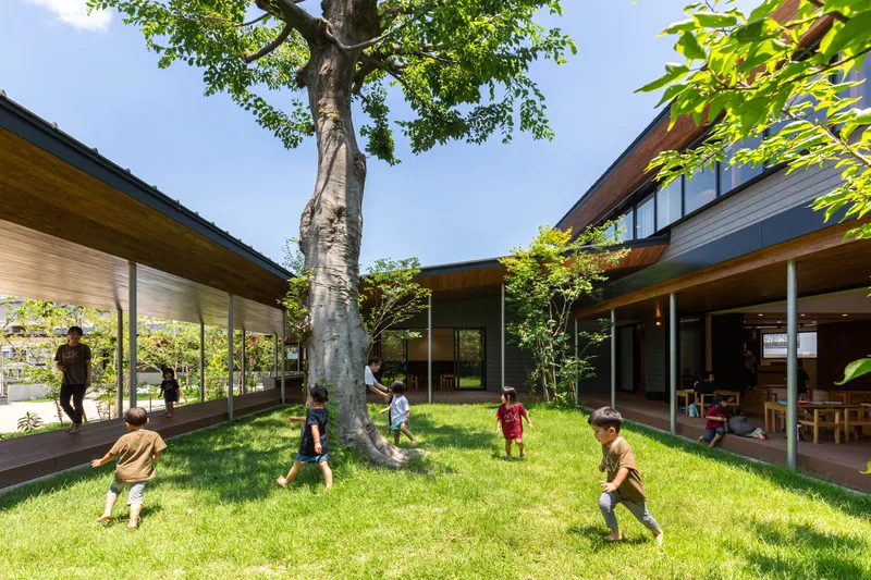 Central courtyard with mature tree and grassy lawn surrounded by low-slung pavilions with children playing