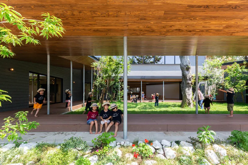 Covered timber deck terrace with slender white columns and planted border with children seated
