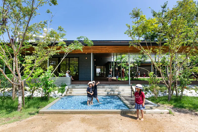 Shallow wading pool with concrete steps and young trees framing the pavilion entrance