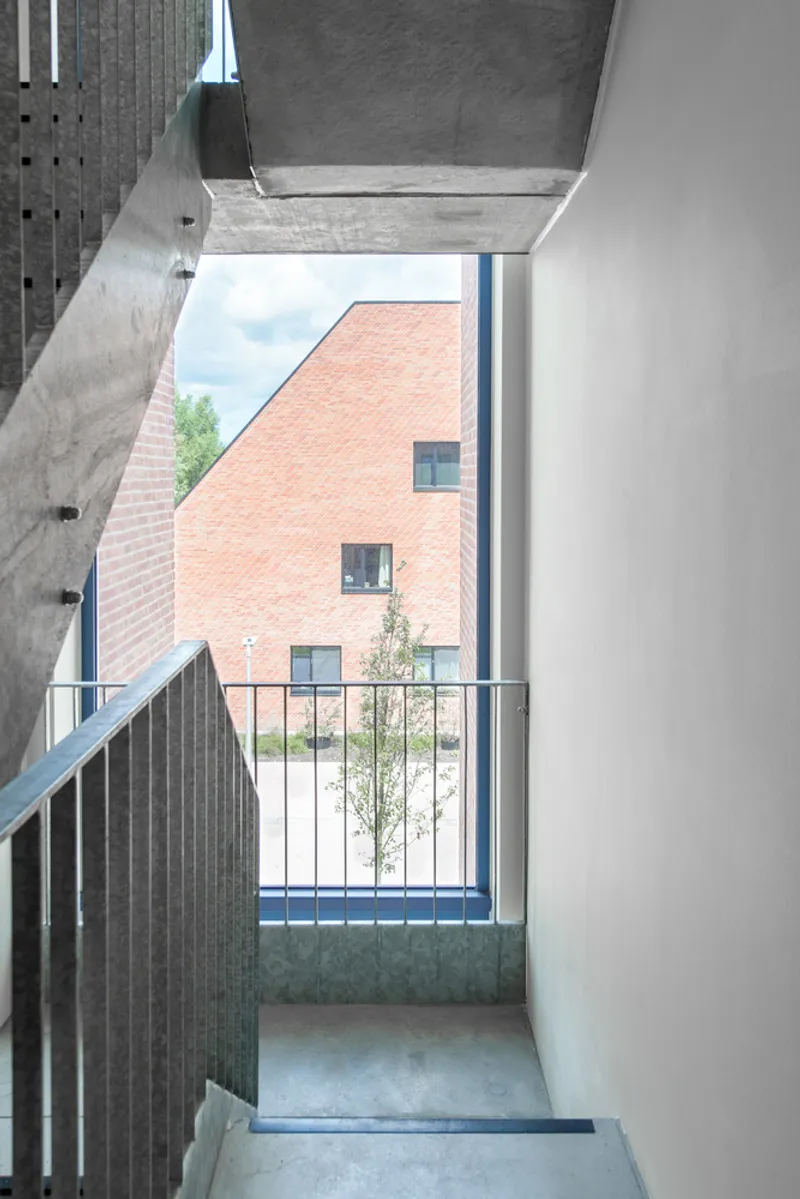 Interior stairwell with slatted timber guard and landing door opening to a pink brick courtyard beyond