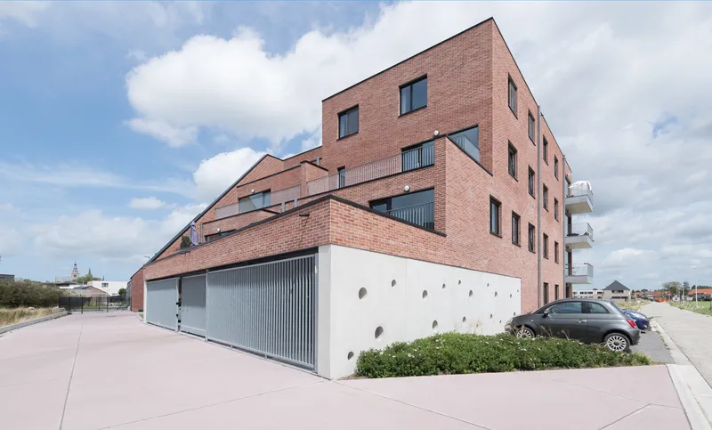 Corner view of the red brick facade with angled volume above white concrete base with circular openings