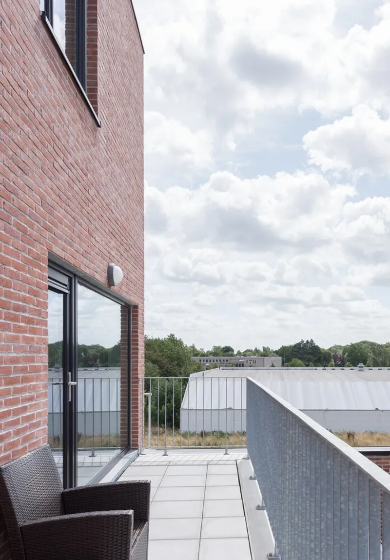 Private terrace with light grey pavers and metal railing looking toward neighboring rooftops under cloudy sky
