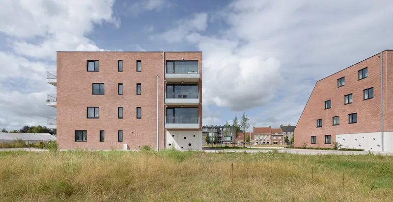 Two brick residential volumes separated by central courtyard space with dry summer grasses in foreground