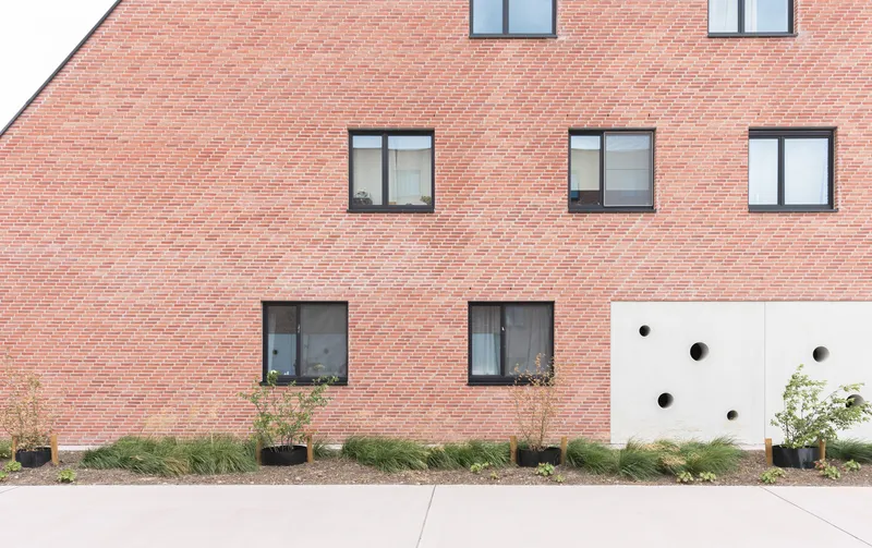 Red brick facade with rectangular windows and white panel punctured by circular openings at ground level