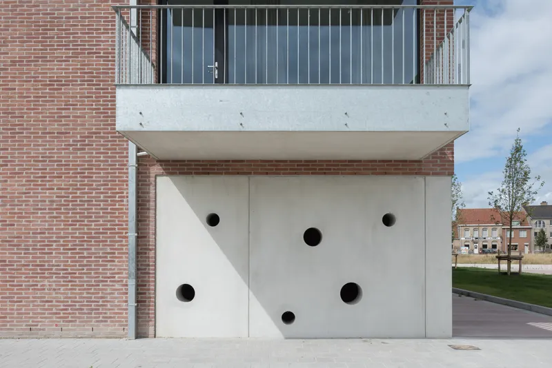 White concrete panel with circular apertures below a cantilevered balcony with vertical metal railings