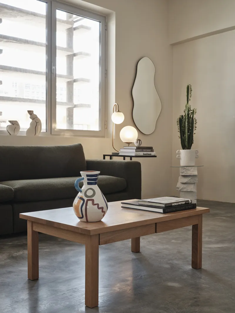 Living area with timber coffee table, dark sofa, and window overlooking concrete columns outside