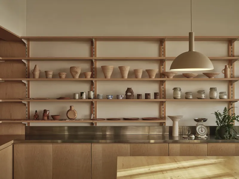 Adjustable timber shelving wall with ceramic display and pendant light above plywood cabinetry and bronze countertop