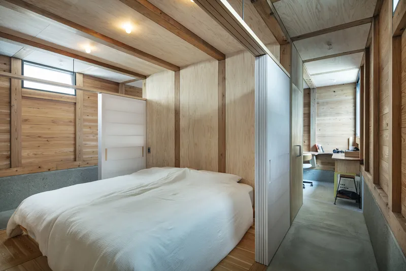 Bedroom with concrete floor and timber frame opening to adjacent study through translucent sliding partition