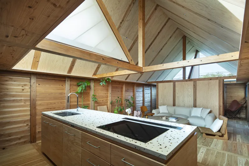 Open kitchen with terrazzo island beneath a vaulted timber ceiling with exposed beams and triangular skylights