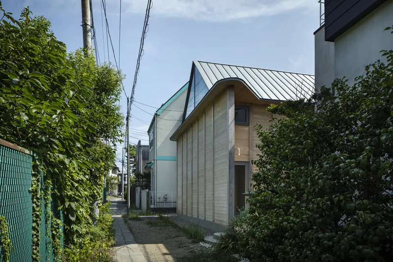 Street view of the timber-clad facade with curved gable and standing seam metal roof between neighboring buildings