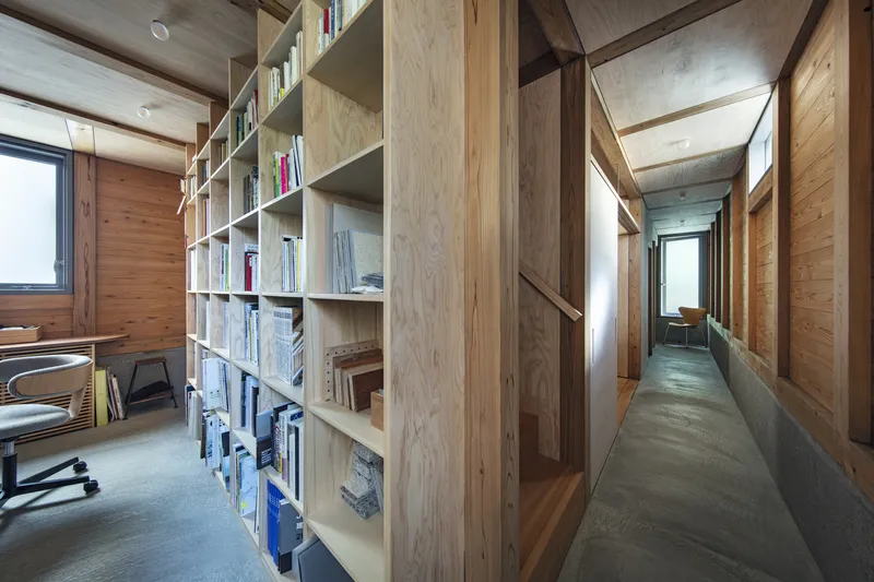 Interior corridor with plywood bookshelf wall and polished concrete floor under pendant lights