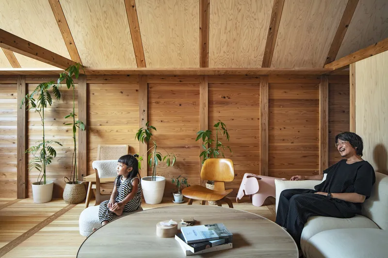 Timber wall lined with structural columns and potted plants alongside inhabitants on a sofa