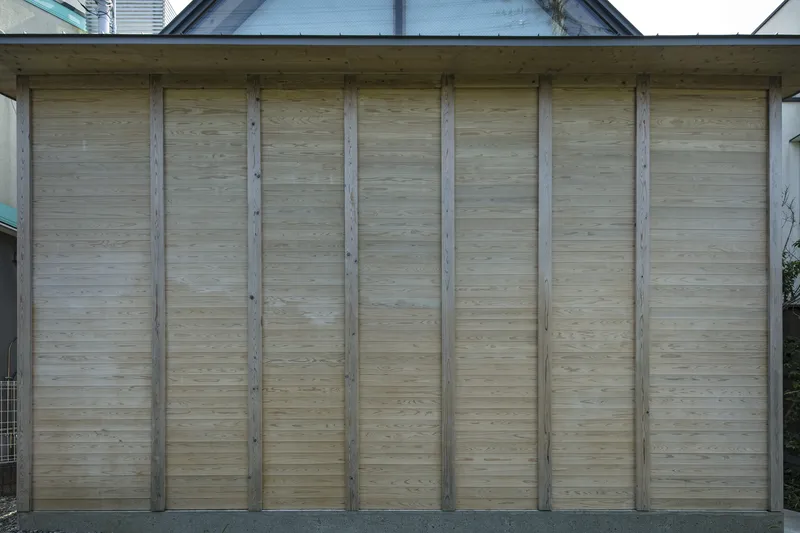 Exterior wall of horizontal bamboo siding between vertical timber structural columns beneath a sheltering roof