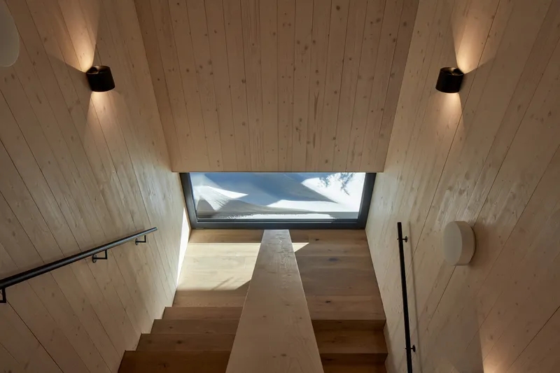 Timber-lined stairwell with skylight above landing and wall-mounted sconces casting upward light