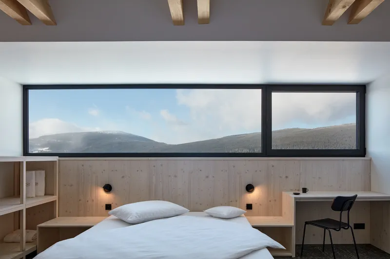 Bedroom with timber headboard and horizontal window framing snow-dusted hills under exposed timber beams