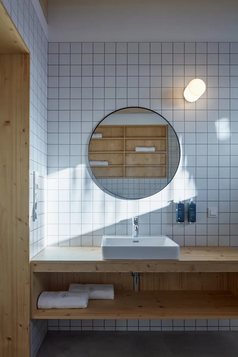White square tile bathroom wall with round mirror above timber vanity and wall-mounted basin