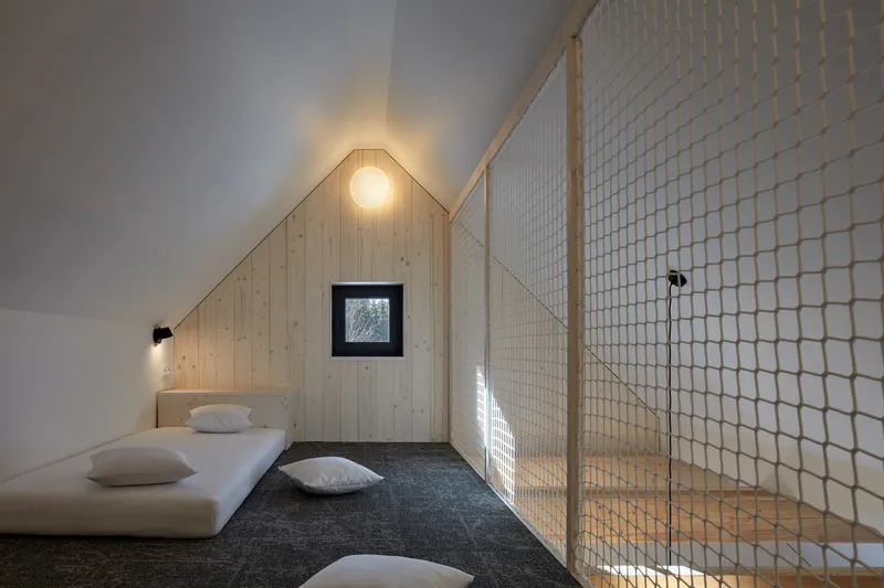 Sleeping loft with rope mesh safety barrier and timber-lined gable wall under a sloped ceiling