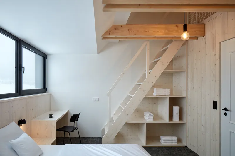 Bedroom loft accessed by a light timber ladder with built-in storage shelves beneath the mezzanine