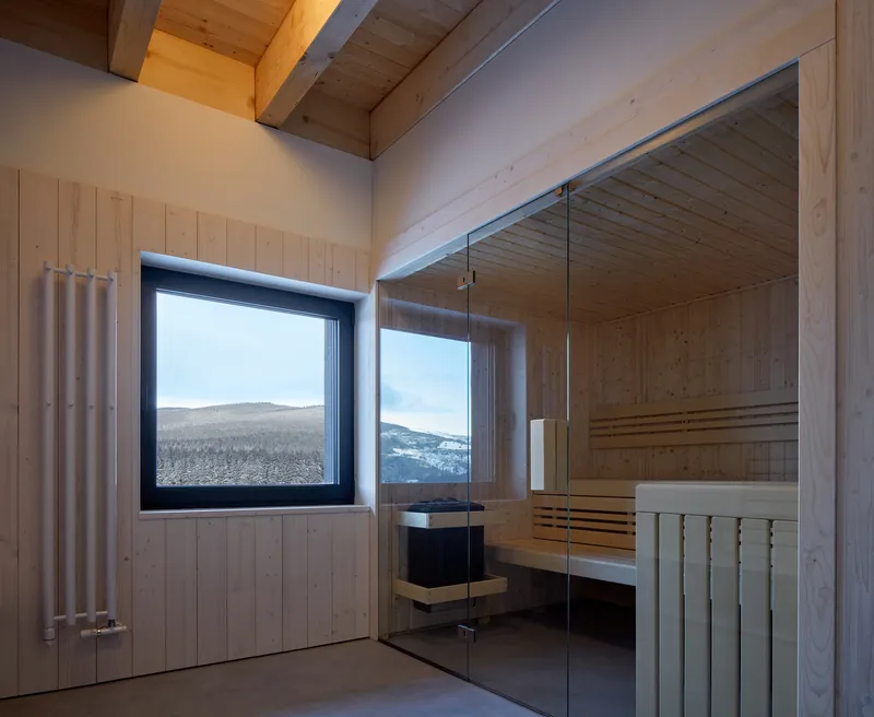 Glass-enclosed sauna with timber benches and window overlooking a winter mountain landscape