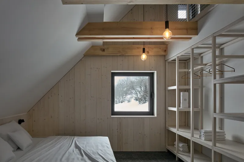 Square window framing a snowy landscape within a timber-clad wall beneath exposed roof beams