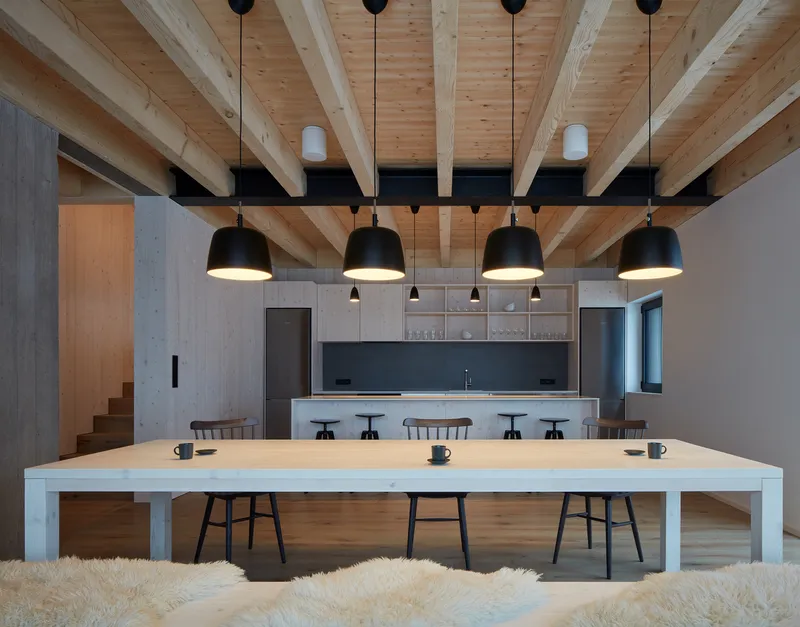 Double-height dining space with exposed timber beams and pendant lights above a long white table