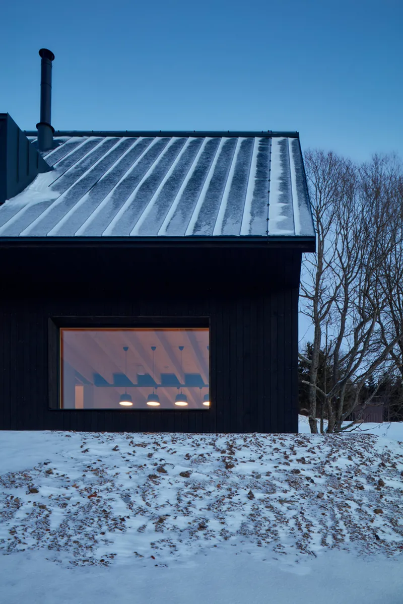 Metal standing seam roof and black timber facade with an illuminated window at twilight