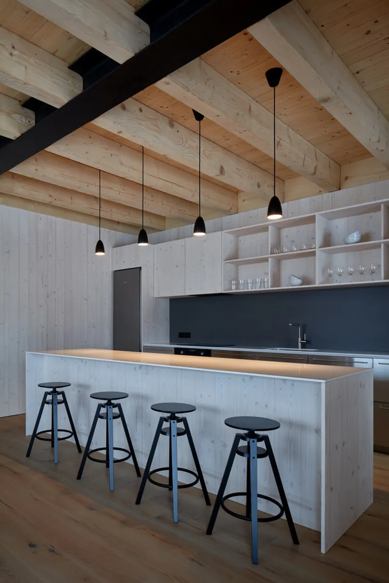 Kitchen island with bar stools beneath exposed timber joists and black pendant lights