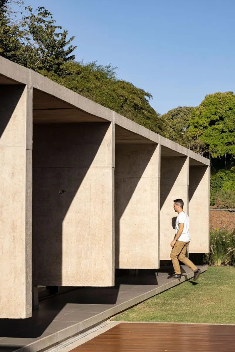 Angled concrete pavilion with sawtooth profile and a figure walking along the timber deck