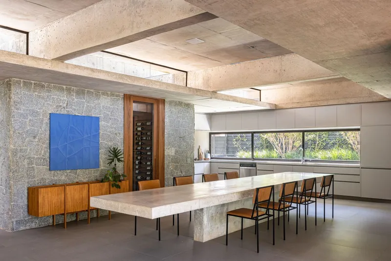 Dining area with travertine table and stone feature wall below geometric concrete coffers