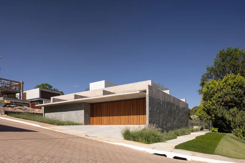 Street facade combining board-formed concrete, timber cladding, and dark stone on a sloped site