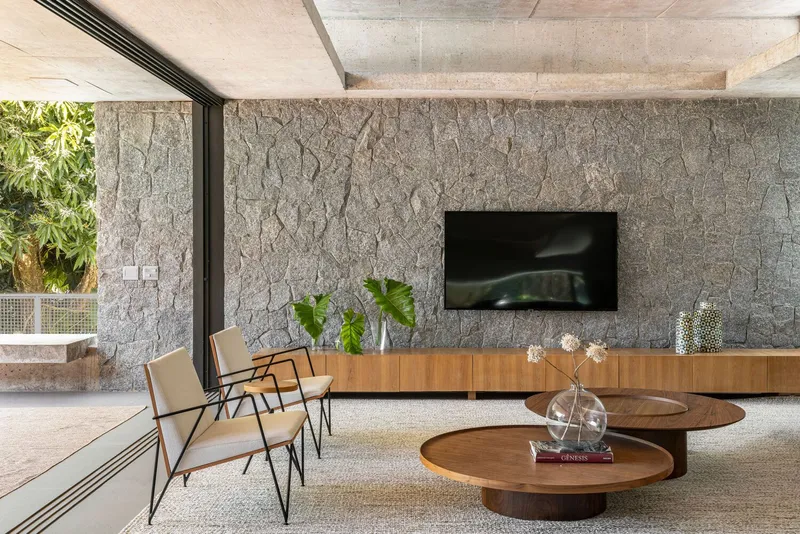 Living room with textured stone accent wall, exposed concrete ceiling beams and sliding glass door to planted garden