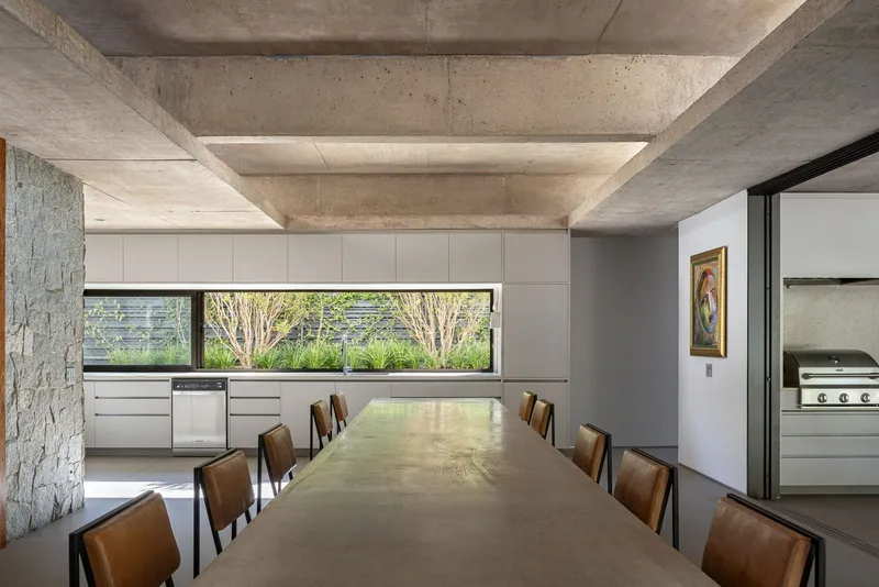 Dining room with coffered concrete ceiling, horizontal window framing garden views and leather dining chairs