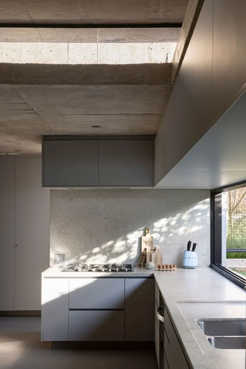 Kitchen island with dappled sunlight filtering through glass onto textured stone backsplash and concrete countertop
