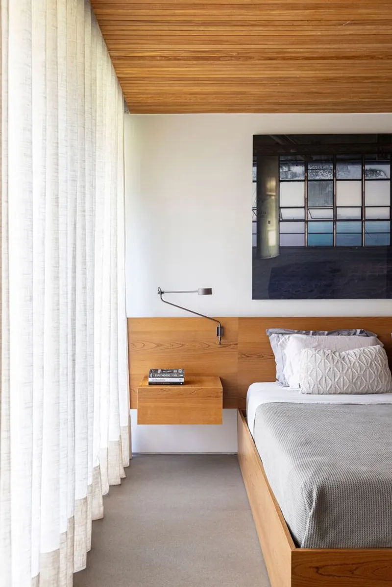 Bedroom with timber platform bed, floating nightstand, timber slat ceiling and sheer curtains filtering daylight