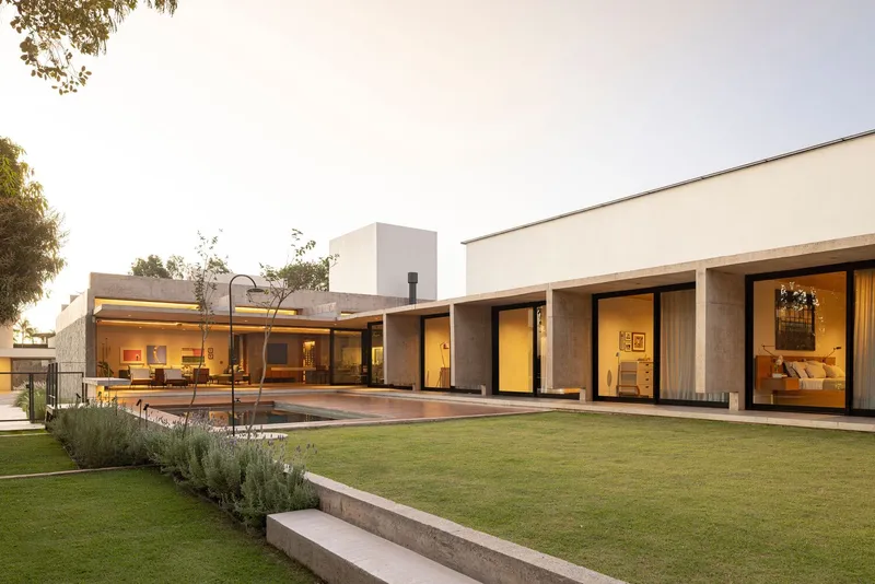 Rear elevation with glass walls and timber columns opening onto lawn and pool terrace at dusk