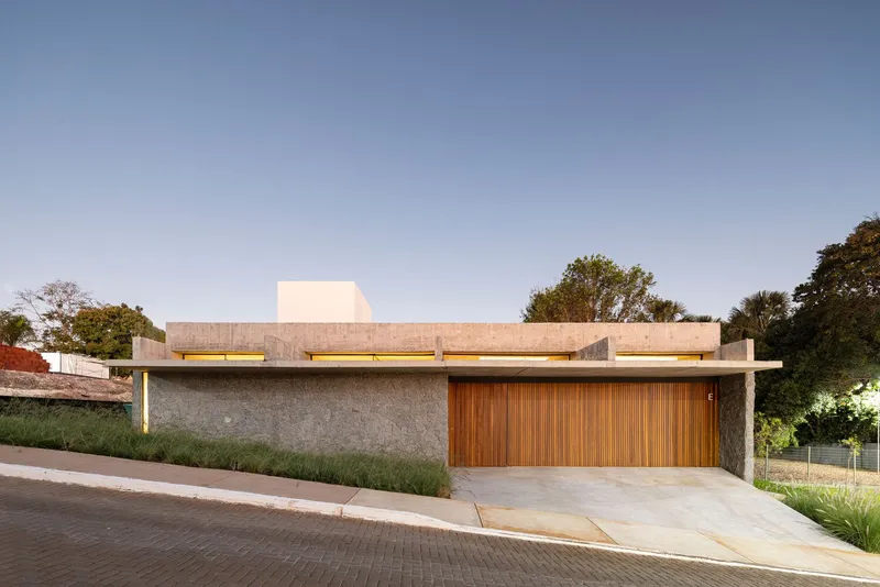 Street facade with timber garage door beneath a wide concrete roof slab and white upper volume