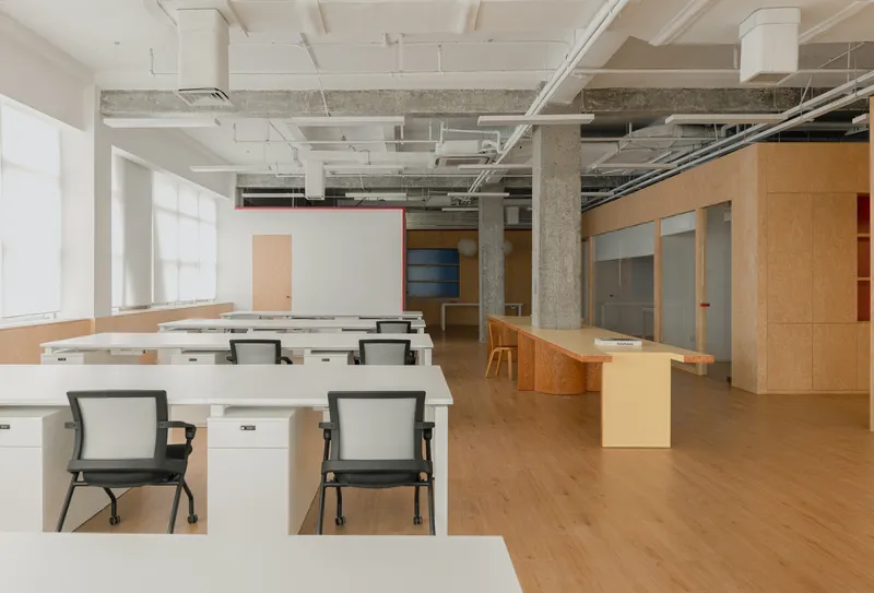 Open office space with exposed concrete columns, white desks and plywood partitions under a coffered ceiling