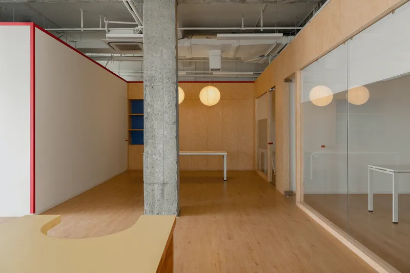 Plywood meeting room with spherical pendant lights and exposed concrete columns in the background