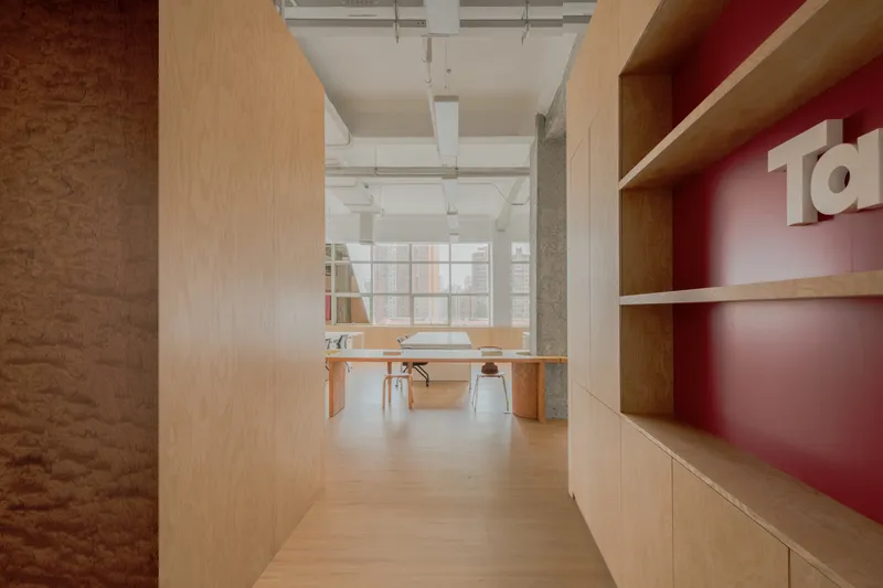 Corridor view framed by plywood walls with red shelving looking toward a glass partition