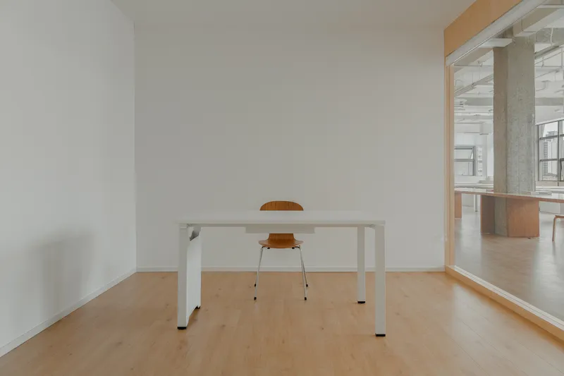 Single white work table with orange chair in a minimal room framed by plywood trim