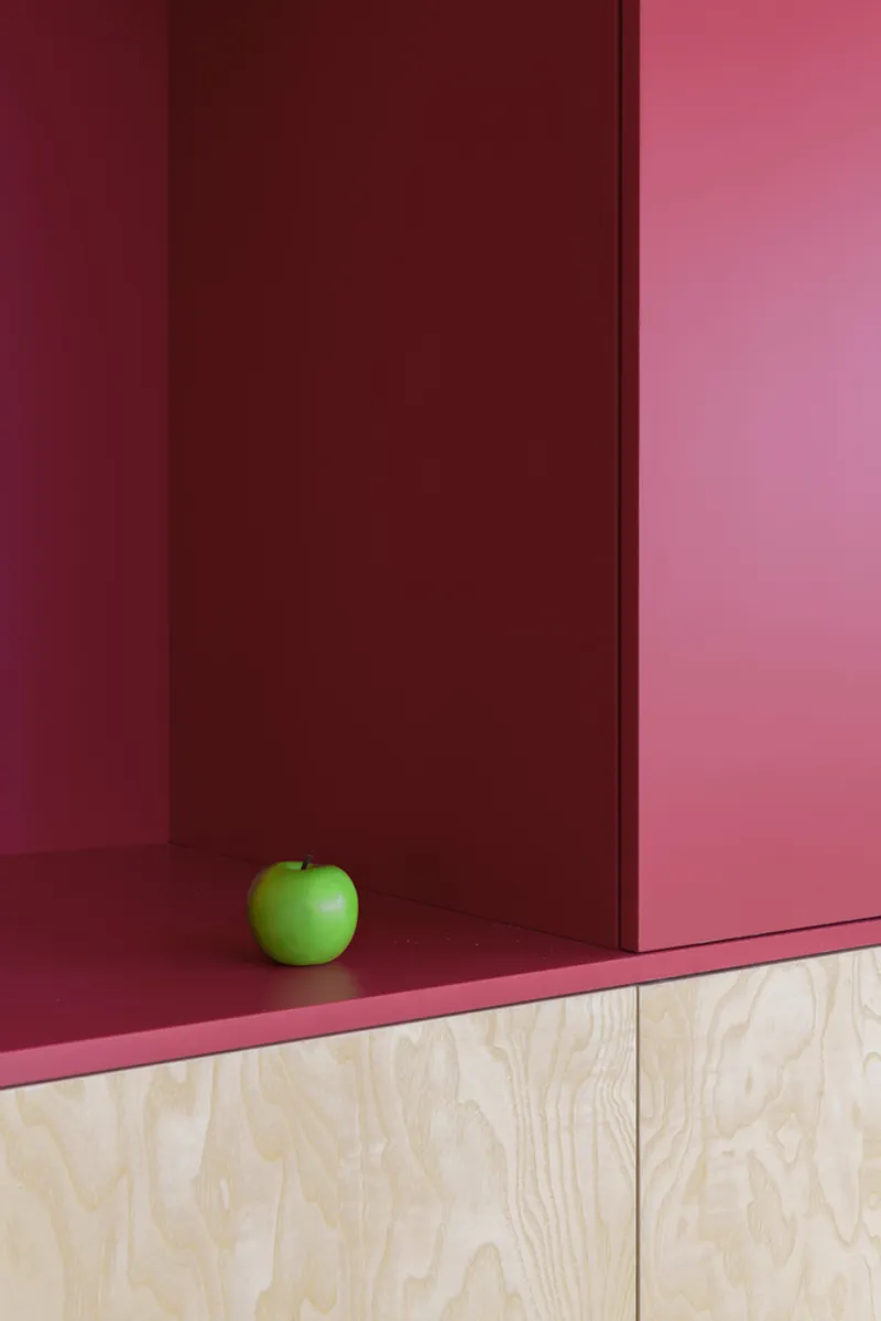 Close-up of a red door panel and pink shelf edge with a green apple