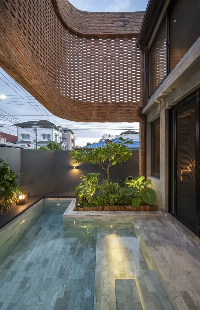 Courtyard pool with planted bed beneath a curving perforated brick overhang at dusk