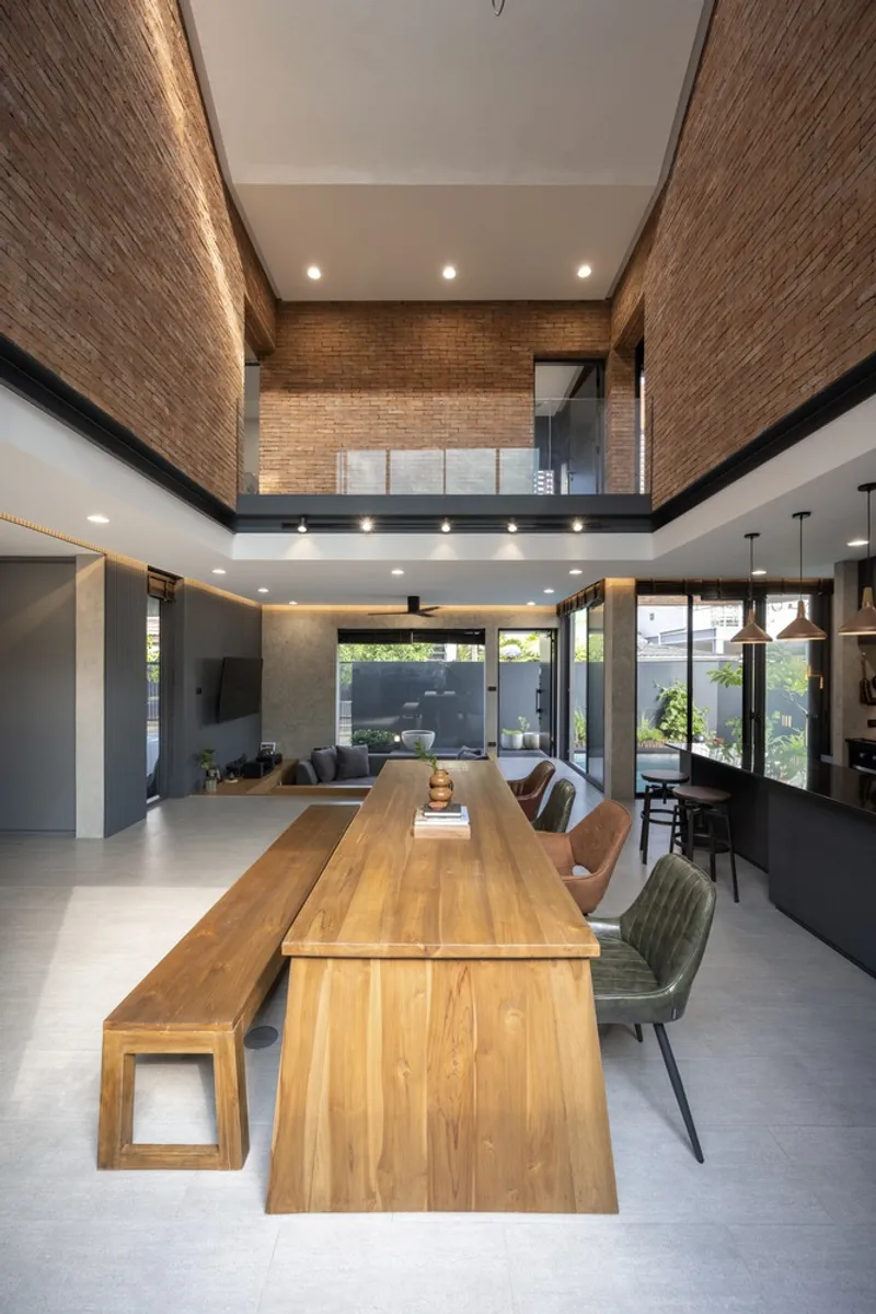 Double-height dining area with timber table and bench beneath a brick-lined void and clerestory windows