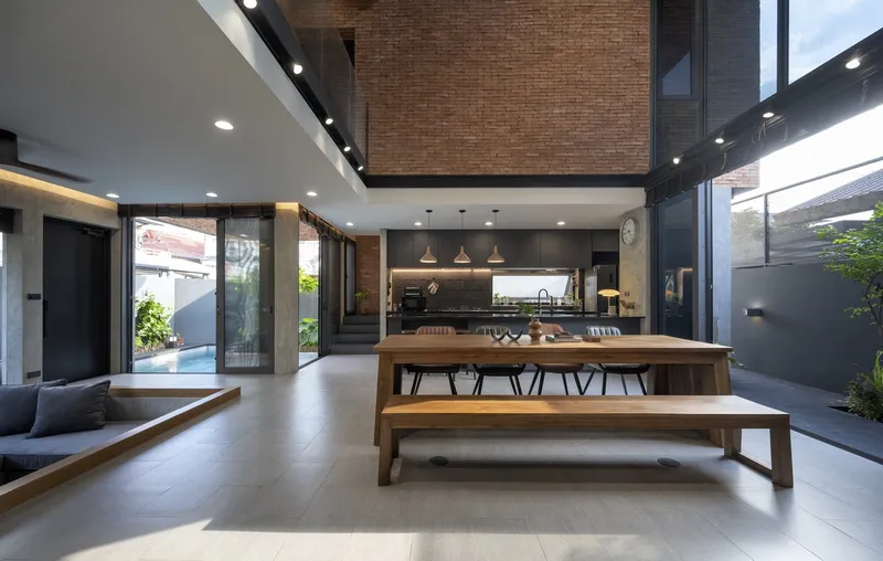 Living and dining area opening to courtyard with suspended brick volume overhead and pendant lights